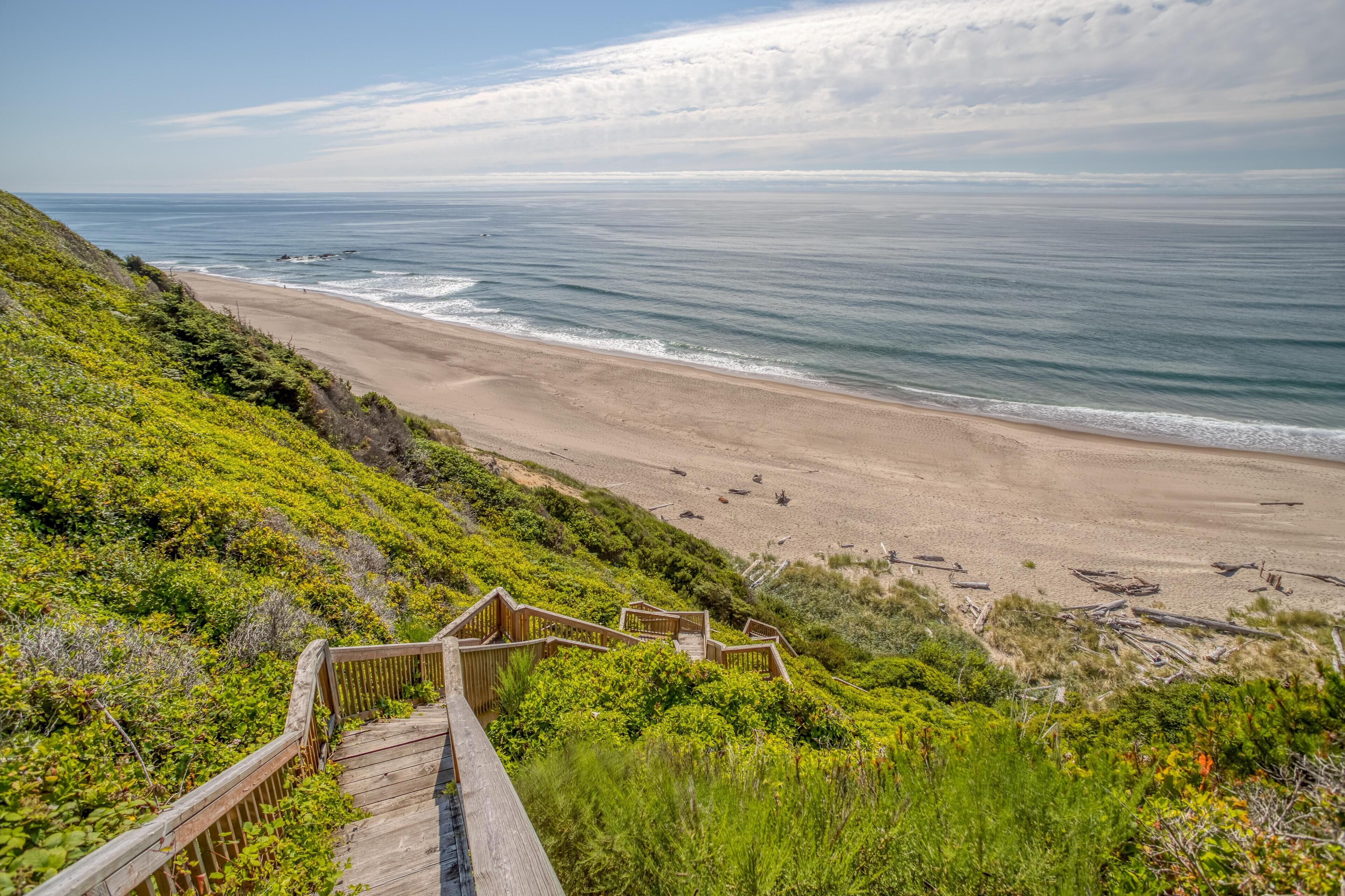 A coastal view with a wooden boardwalk leading to a sandy beach.