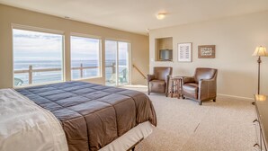 A bedroom with a large bed, two chairs, a small table, and a TV. - Storm Watchers Pointe (Lincoln City)