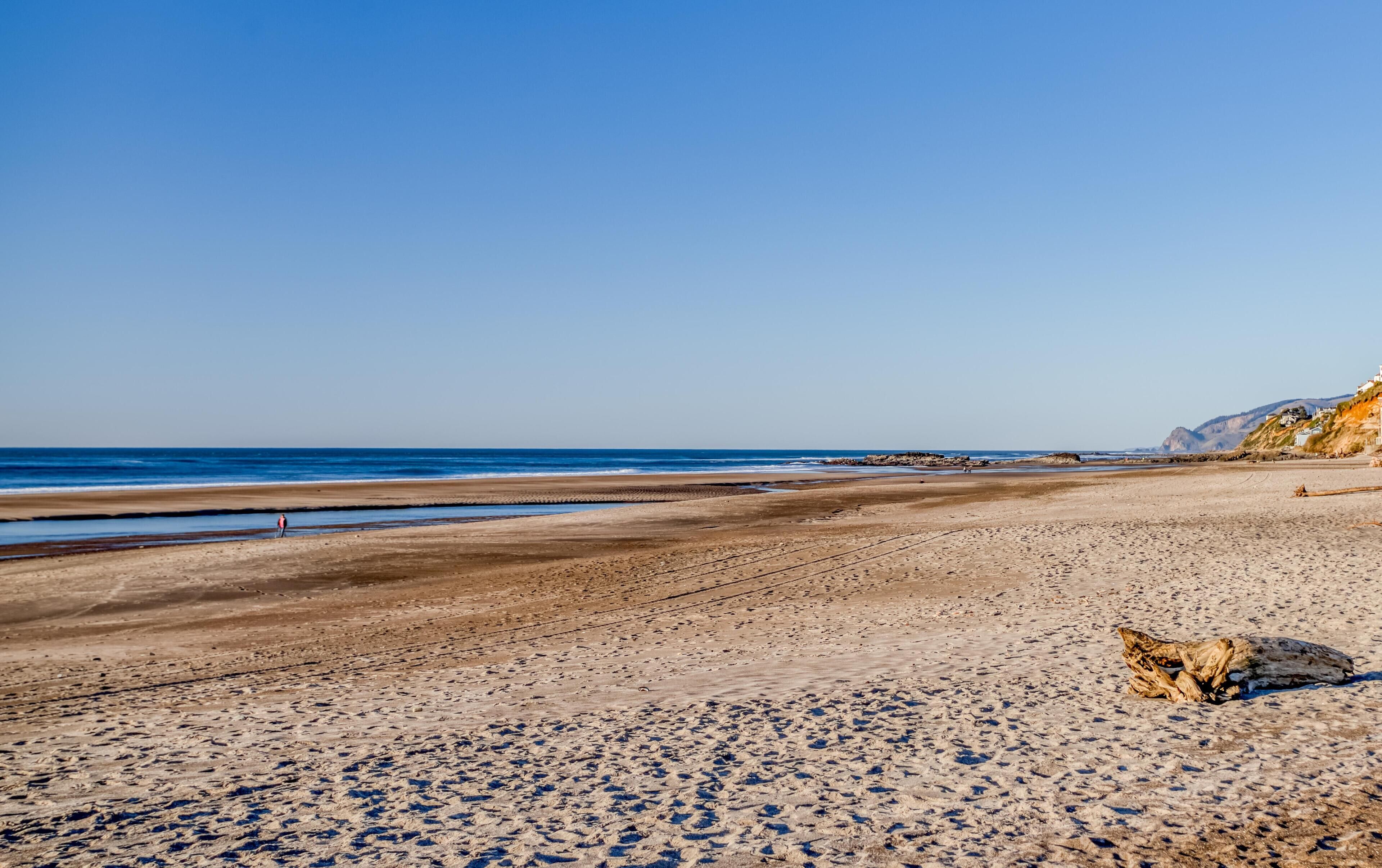 Ein weiter Strand mit blauem Himmel, Felsen und einigen Spaziergängern.
