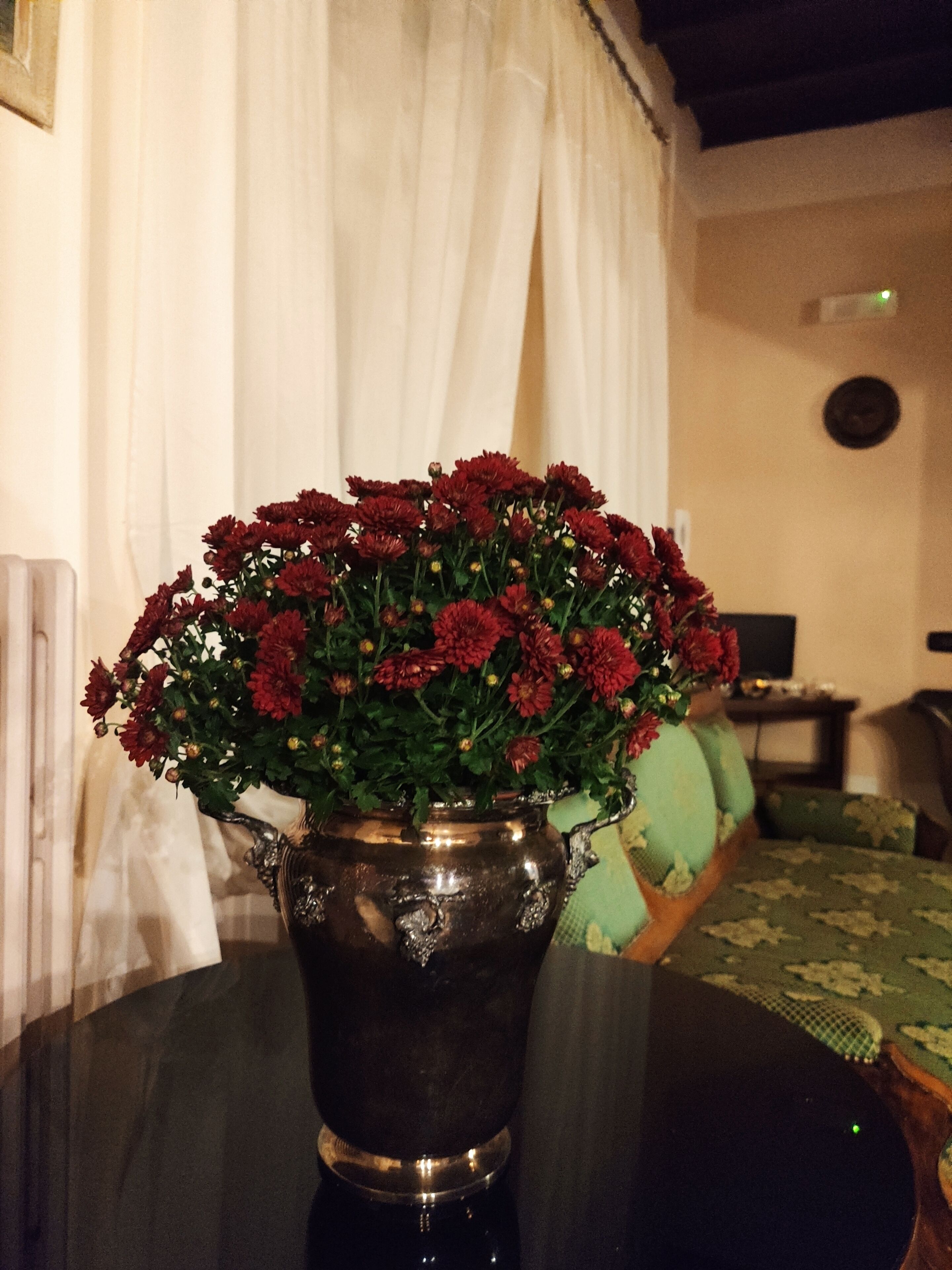 Een tafel met een metalen vaas gevuld met rode bloemen.