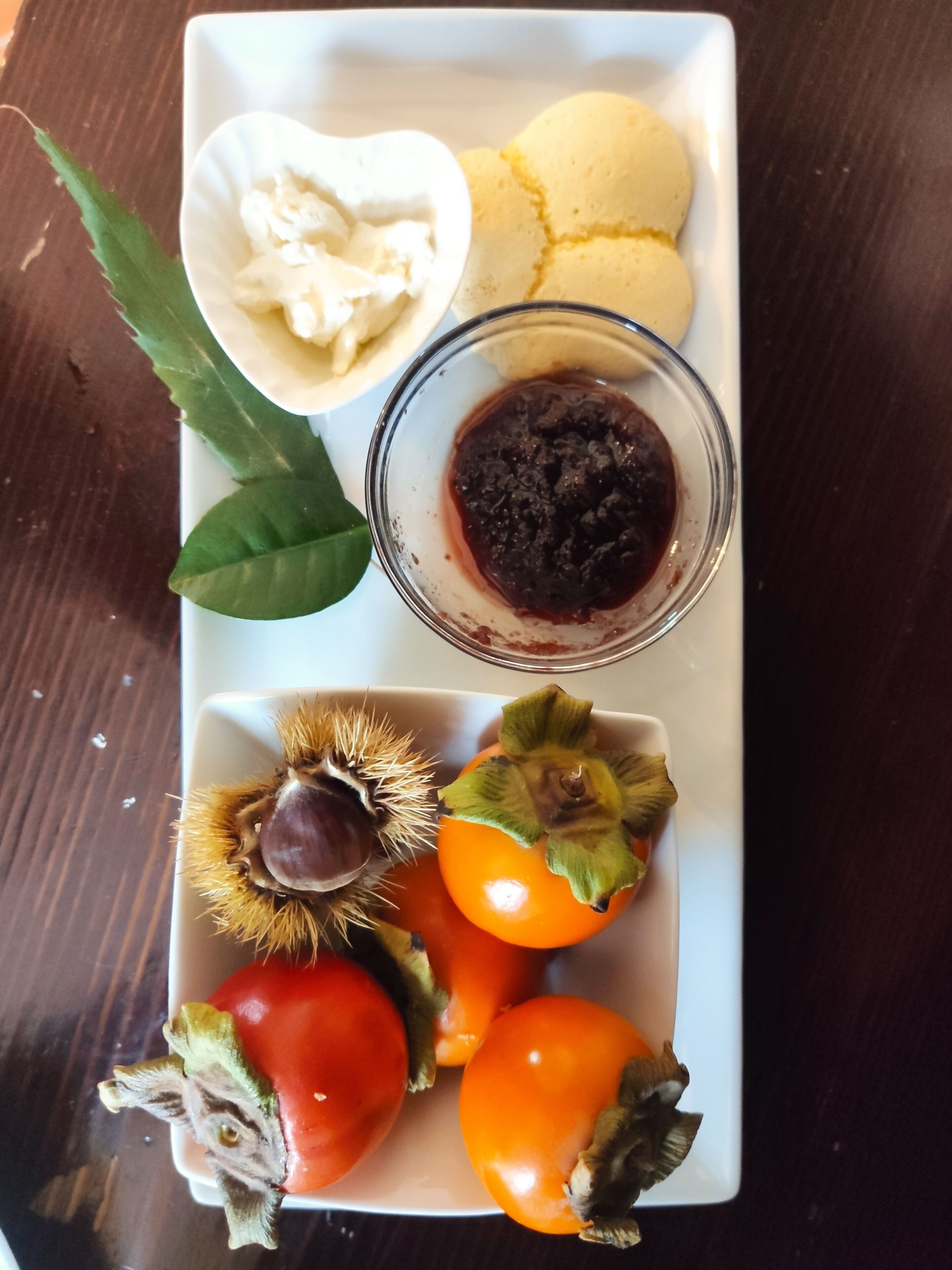 Un plato blanco con diversos alimentos, incluyendo un bol de crema batida, un bol de salsa oscura y varios tomates con rabo.
