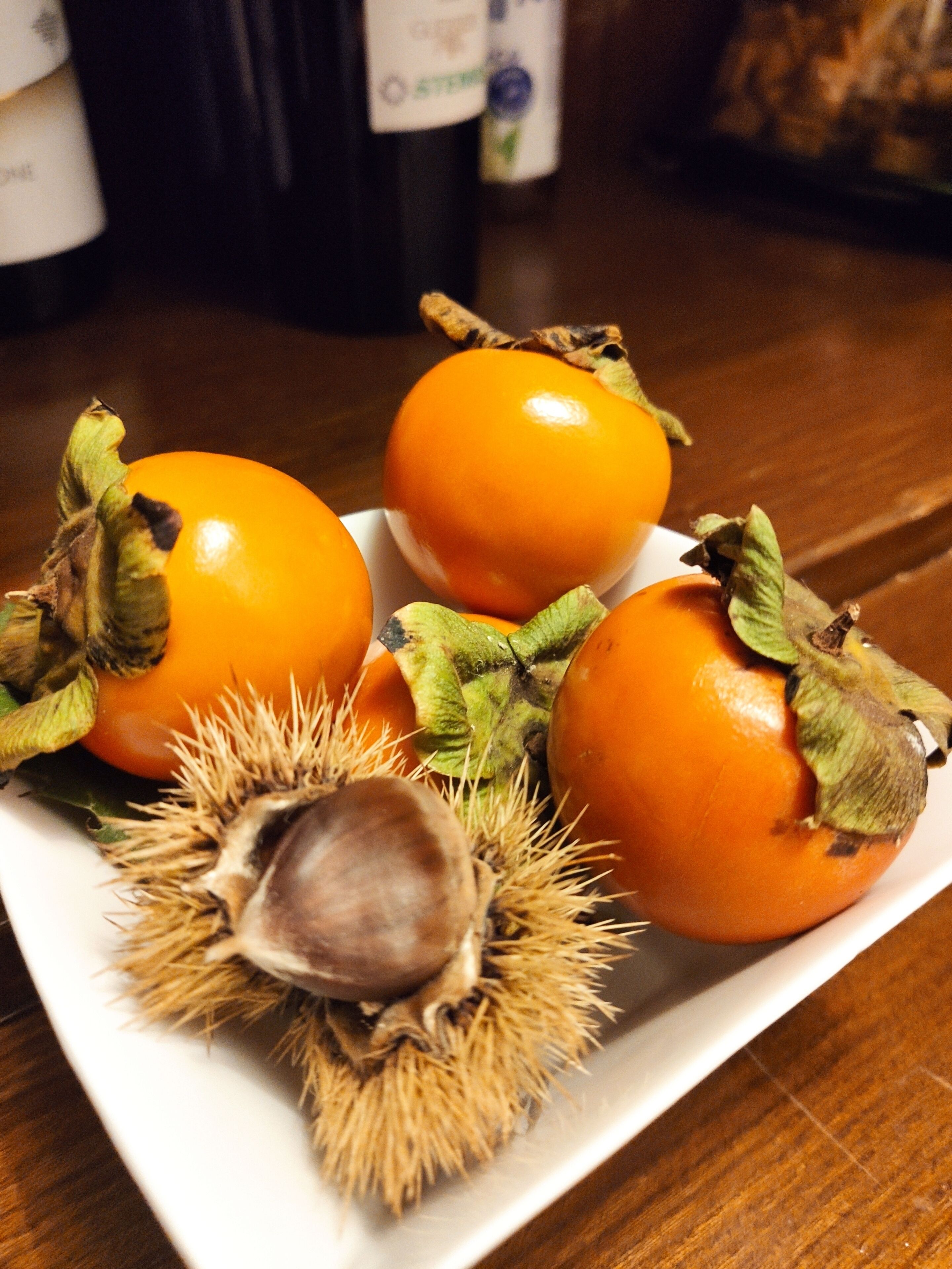A plate with three persimmons and a chestnut.