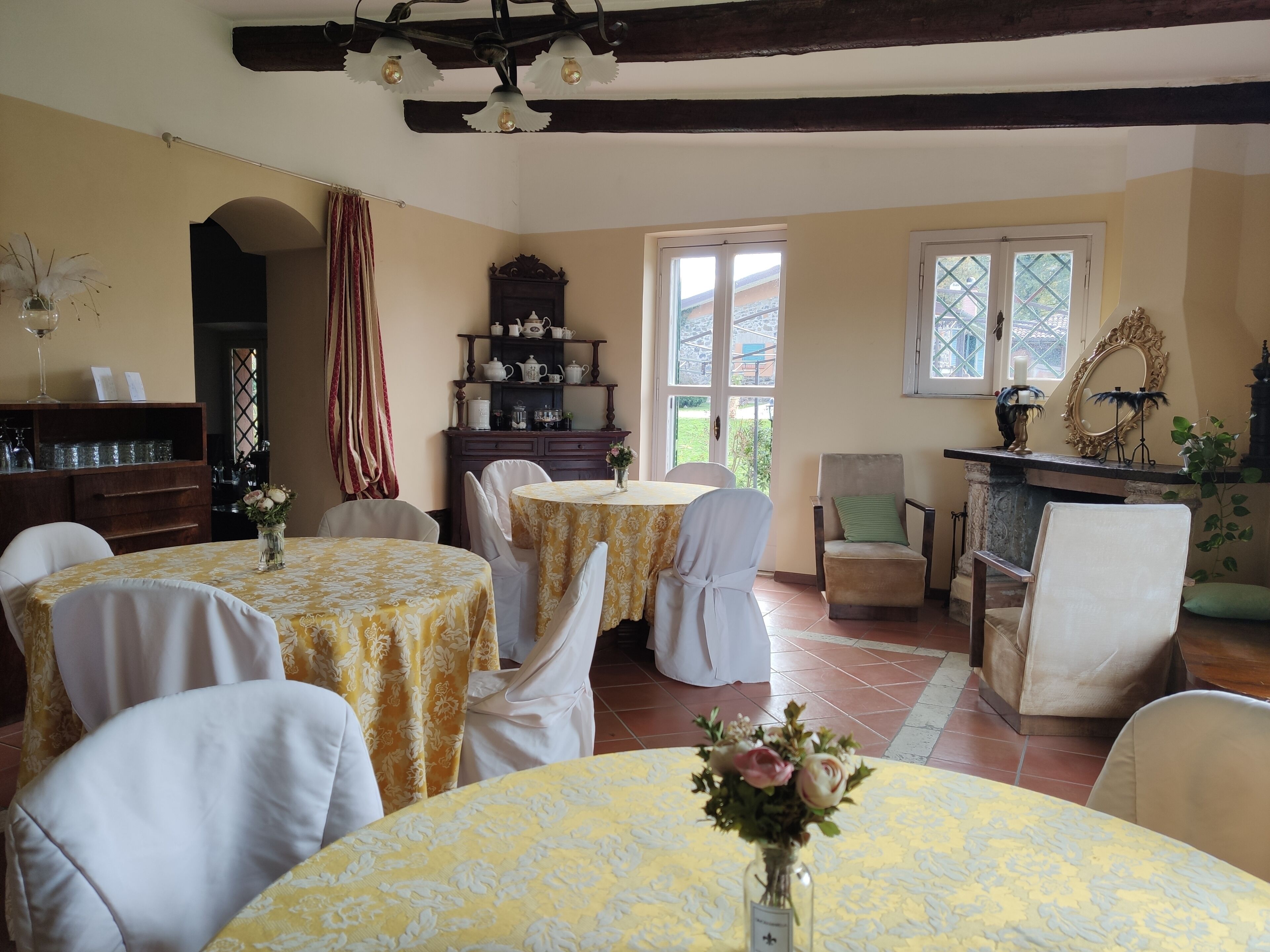 A dining area with round tables covered in yellow tablecloths, white chairs, and a wooden cabinet with kitchenware.