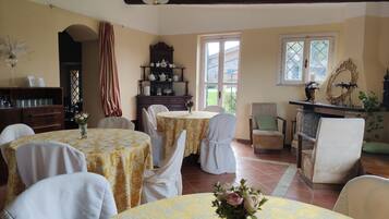 A dining area with round tables covered in yellow tablecloths, white chairs, and a wooden cabinet with kitchenware.