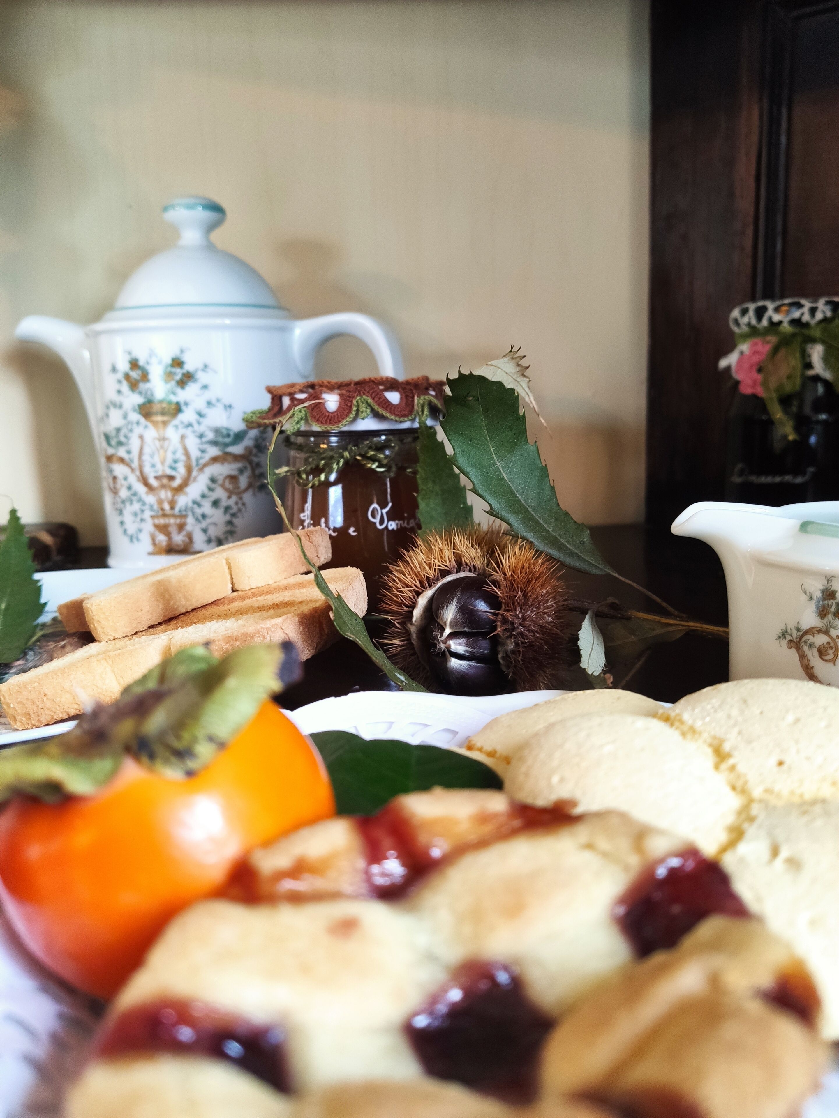 Une table mise avec une théière, un bocal en verre, du pain et une composition de fruits.