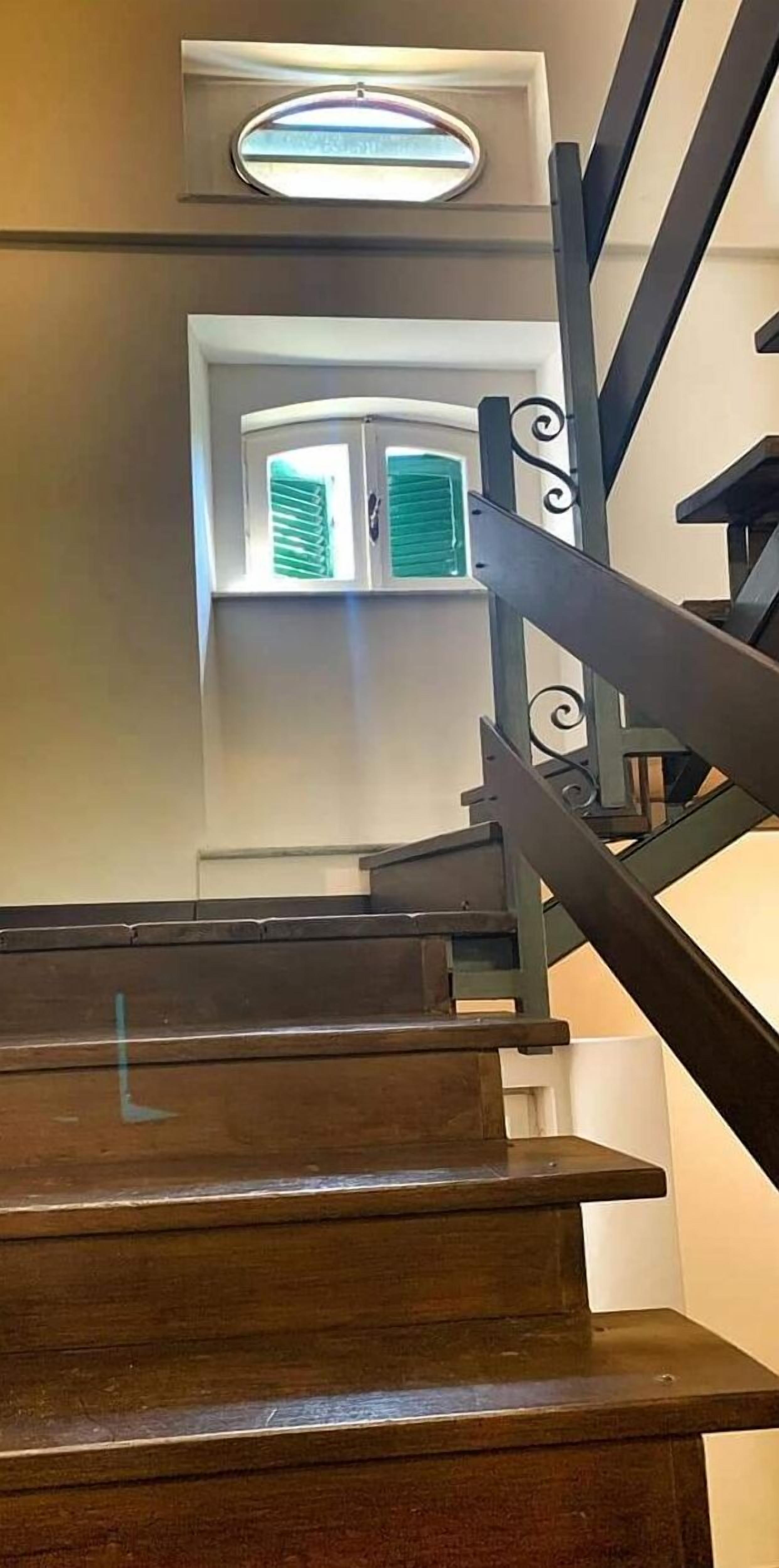 A wooden staircase with a handrail and a window with green shutters.