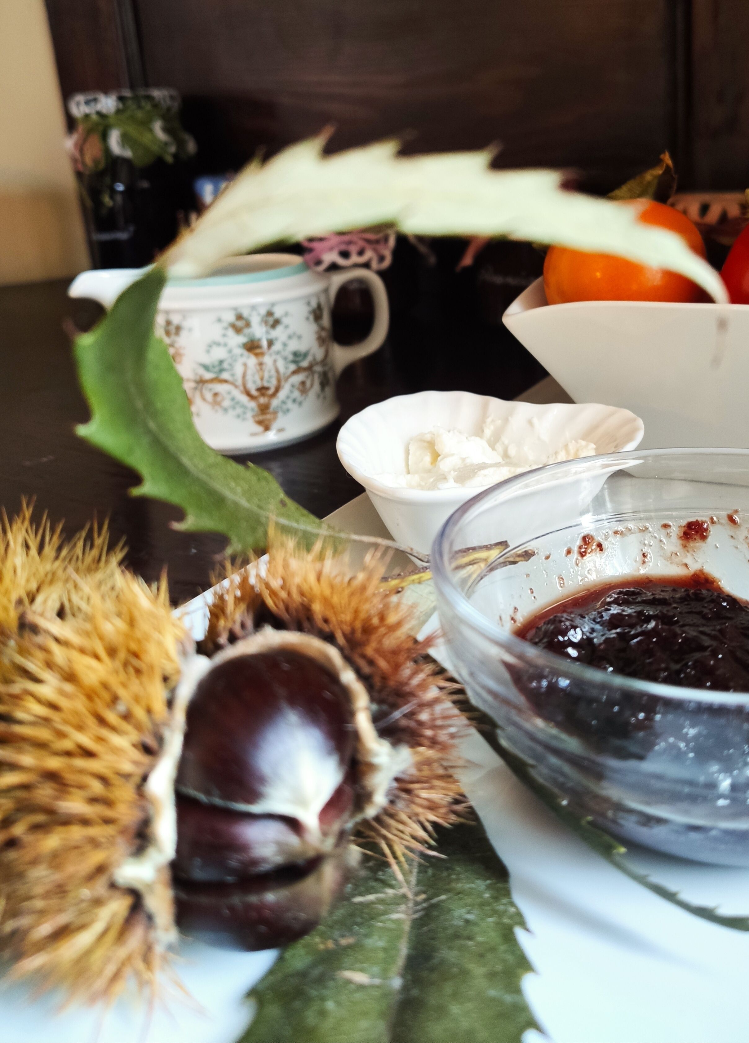 Ein Esstisch mit einer Schale Kastanien, einer Marmeladenschale und einer Tasse Tee.