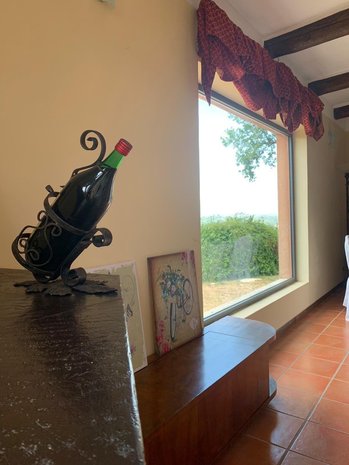 A room with a rustic wooden counter, a decorative bottle sculpture, a framed artwork, and a window with a view of greenery.