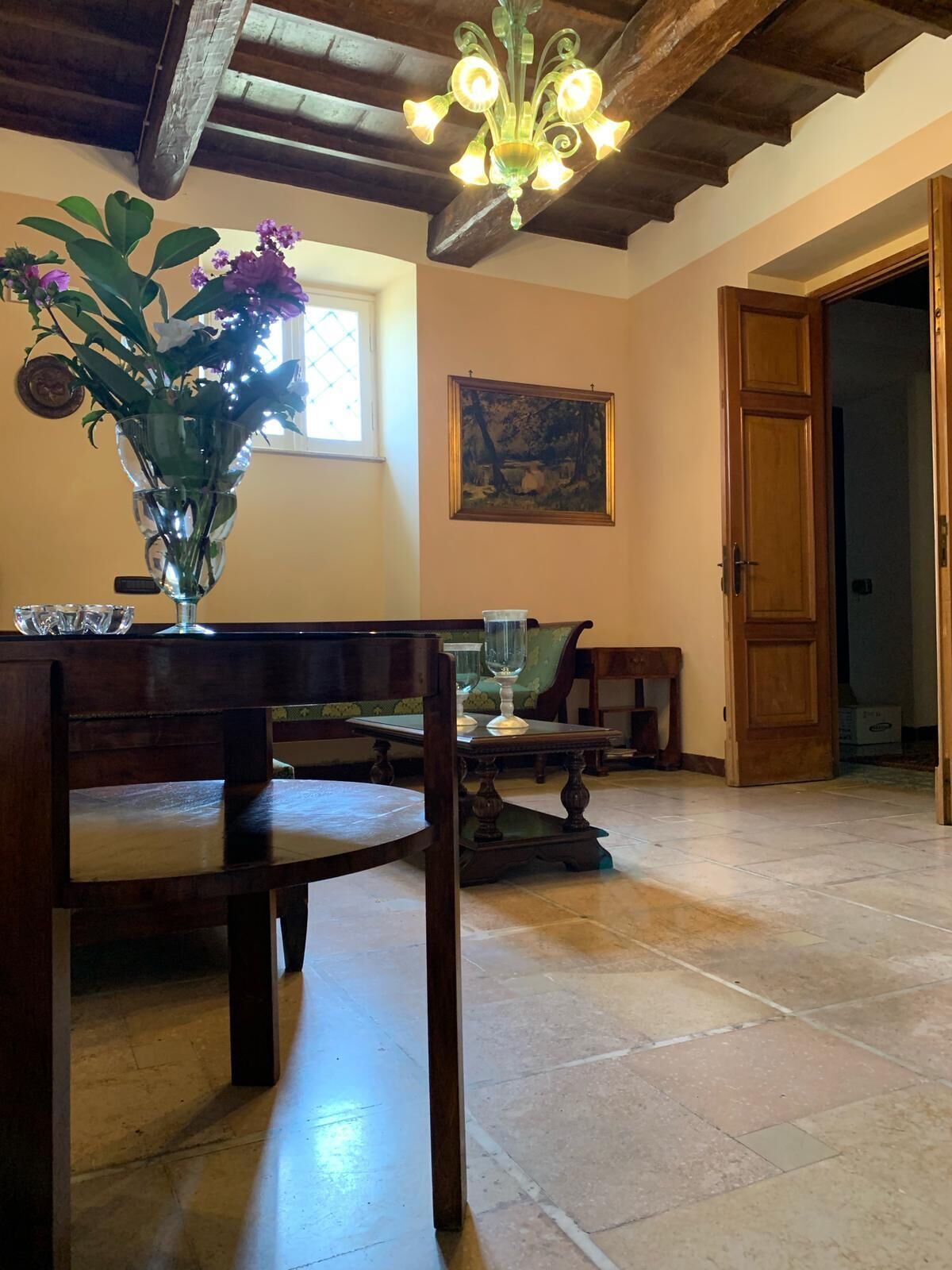 Una habitación con una mesa de comedor de madera, sillas, un florero con flores, un cuadro en la pared y una puerta de madera.