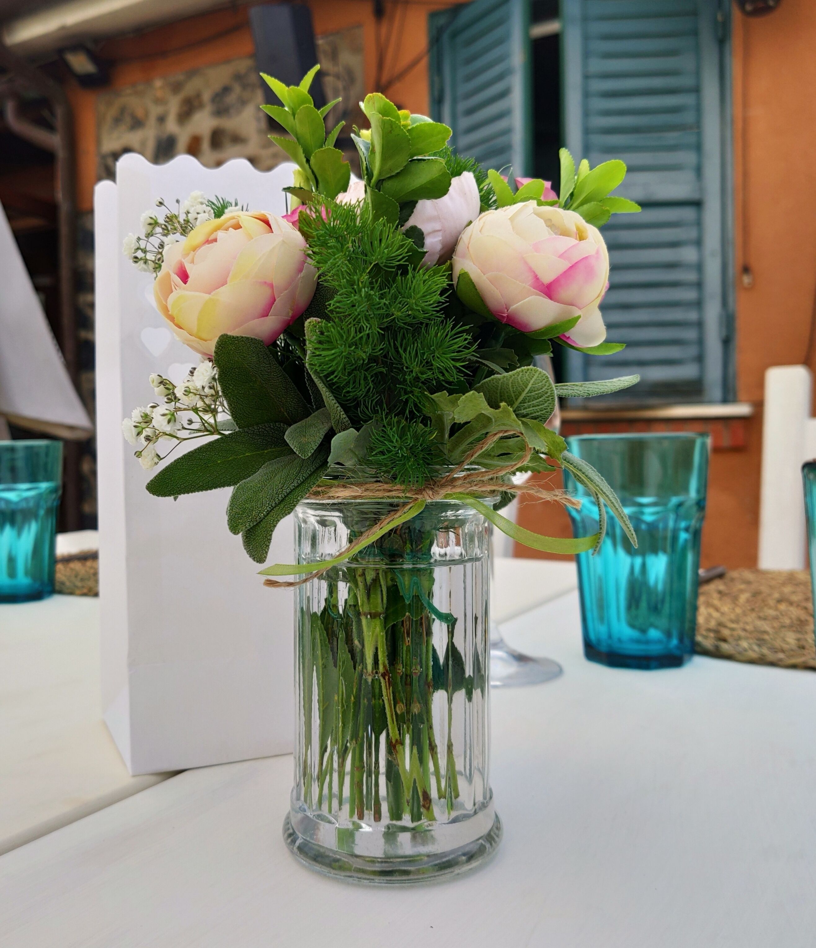 Un vase en verre transparent contenant un bouquet de fleurs et de verdure, posé sur une table.