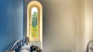 A bedroom with a bed, a nightstand, a lamp, and a window with a view of greenery.