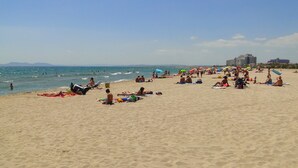 A sandy beach with people sunbathing and swimming. - Rubina Resort (Castello d'Empuries)
