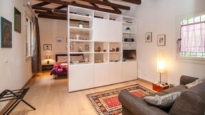 A cozy living room with a built-in white shelving unit, a comfortable sofa, a patterned rug, and a bed with a pink bedspread.