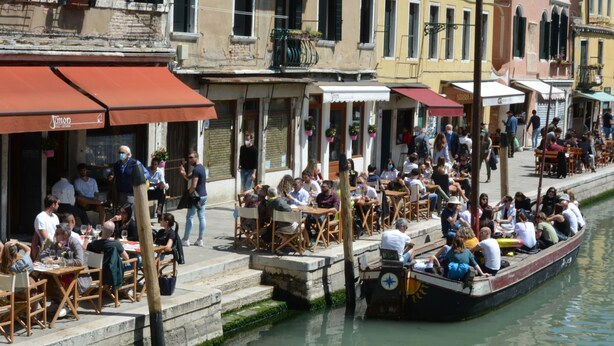 A canal-side restaurant with outdoor seating, a gondola, and a row of colorful buildings.