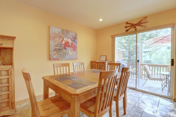 A dining area with a wooden table and chairs, a painting on the wall, and a sliding glass door leading to an outdoor patio.