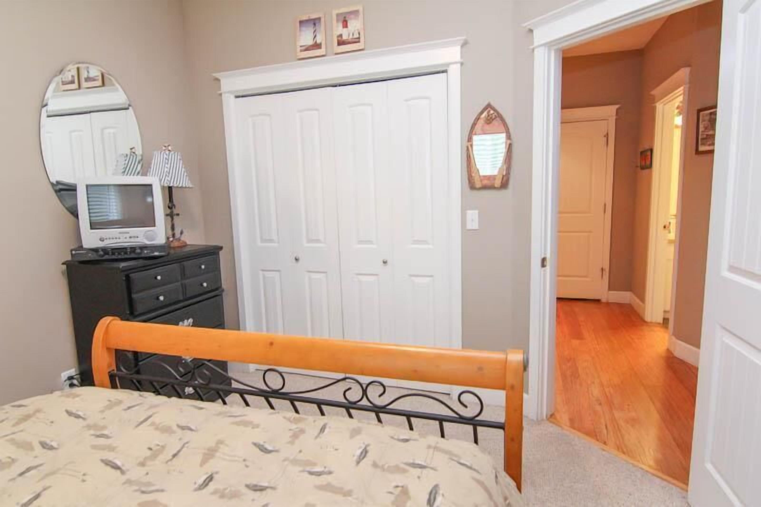 A bedroom with a bed, dresser, mirror, and a white wardrobe.