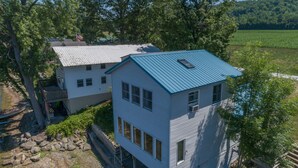 Une maison à deux étages, avec un toit bleu, entourée d’arbres et d’un champ.