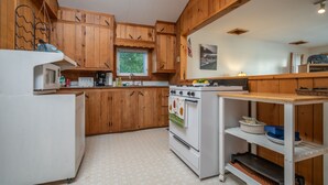 Une cuisine avec des meubles de rangement en bois, un réfrigérateur blanc, une cuisinière et une petite étagère où sont rangés de la vaisselle.