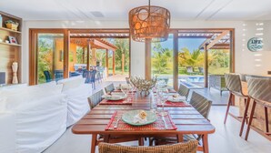 Un coin repas avec une table en bois dressée pour le repas, entourée de chaises en osier, et un grand luminaire suspendu.