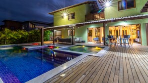Une maison à deux étages avec une piscine, du mobilier d’extérieur et une terrasse en bois.