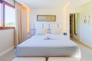 A modern hotel room with a large bed, a bedside table, a nightstand, a framed artwork above the bed, and a view of the outdoors through the window.