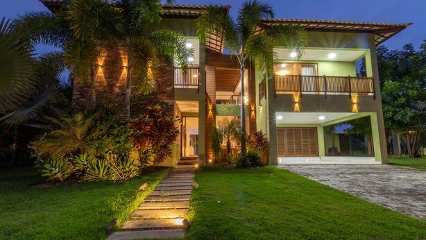 Une maison à deux étages dotée d’un balcon, entourée d’une végétation luxuriante et d’une pelouse bien entretenue.