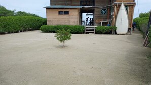 A building with a wooden exterior, a small tree in the center, and a surfboard leaning against the building. - Baru Punta Blanca (Cartagena)