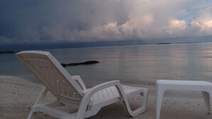 A beach with a white plastic lounge chair and a small table, overlooking calm waters and a cloudy sky. - Baru Punta Blanca (Cartagena)