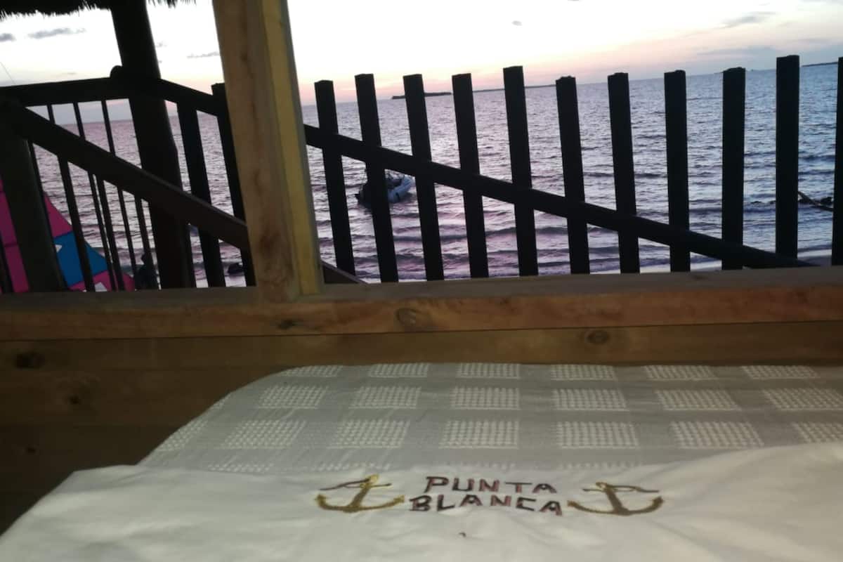 A wooden deck with a railing overlooking a beach. The text "PUNTA BLANCA" is visible on a white fabric.
