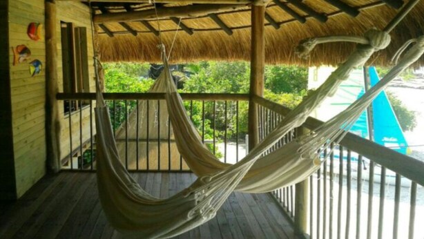 A hammock on a wooden deck with a thatched roof, overlooking greenery. - Baru Punta Blanca (Cartagena)