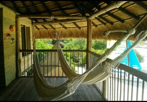 A hammock on a wooden deck with a thatched roof, overlooking greenery. - Baru Punta Blanca (Cartagena)