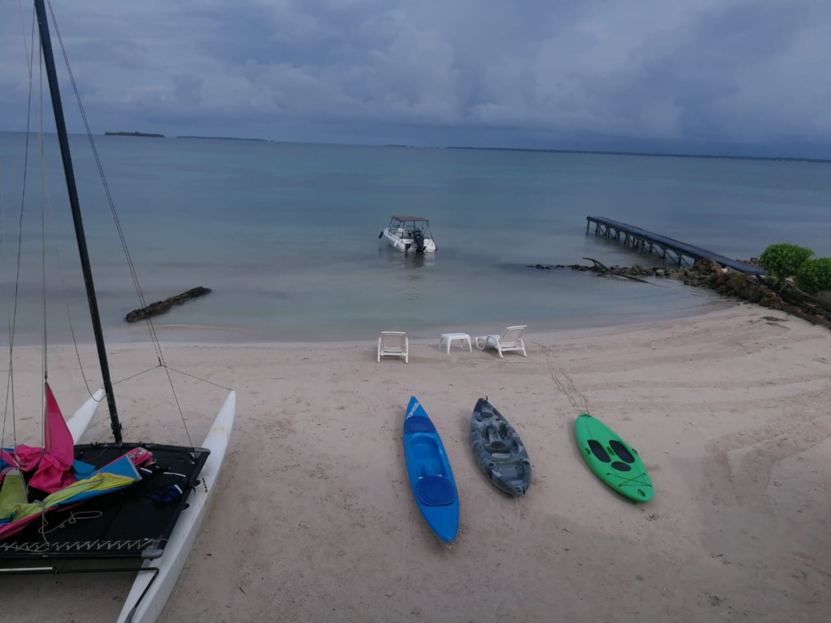 Una playa con kayaks, sillas de descanso y un muelle que se extiende sobre aguas tranquilas.