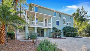 A two-story house with a front porch, a covered entryway, and a driveway. - 6 bd 4 and one half bath Family Friendly Beach Home with heated pool Just a block to the beach (Hilton Head Island)