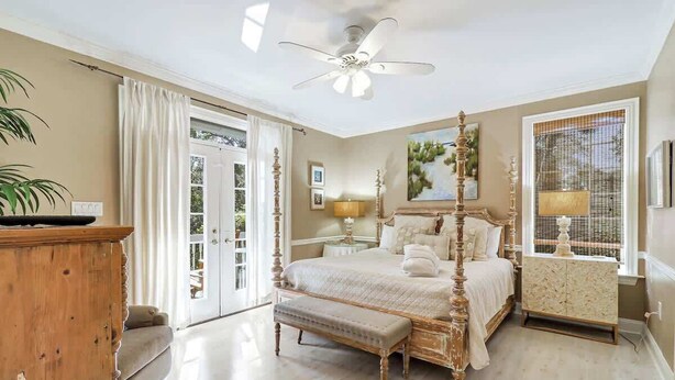 A bedroom with a four-poster bed, a wooden bench, a nightstand, and a window with a view. - 6 bd 4 and one half bath Family Friendly Beach Home with heated pool Just a block to the beach (Hilton Head Island)