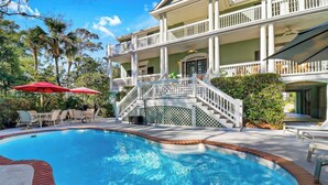 A pool area with a brick border, a red umbrella, and outdoor furniture. - 6 bd 4 and one half bath Family Friendly Beach Home with heated pool Just a block to the beach (Hilton Head Island)