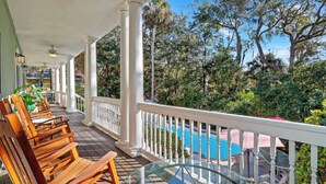 A covered outdoor area with wooden chairs and a glass table, overlooking a swimming pool and lush greenery. - 6 bd 4 and one half bath Family Friendly Beach Home with heated pool Just a block to the beach (Hilton Head Island)