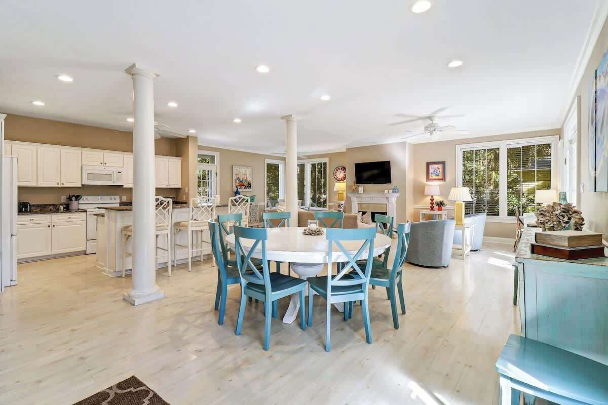 A spacious kitchen with white cabinets, a central island, and a dining area with blue chairs.