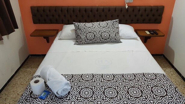 A hotel room with a bed, a patterned throw, a towel, and a remote control on a nightstand. - Hotel Atlantico (Veracruz)