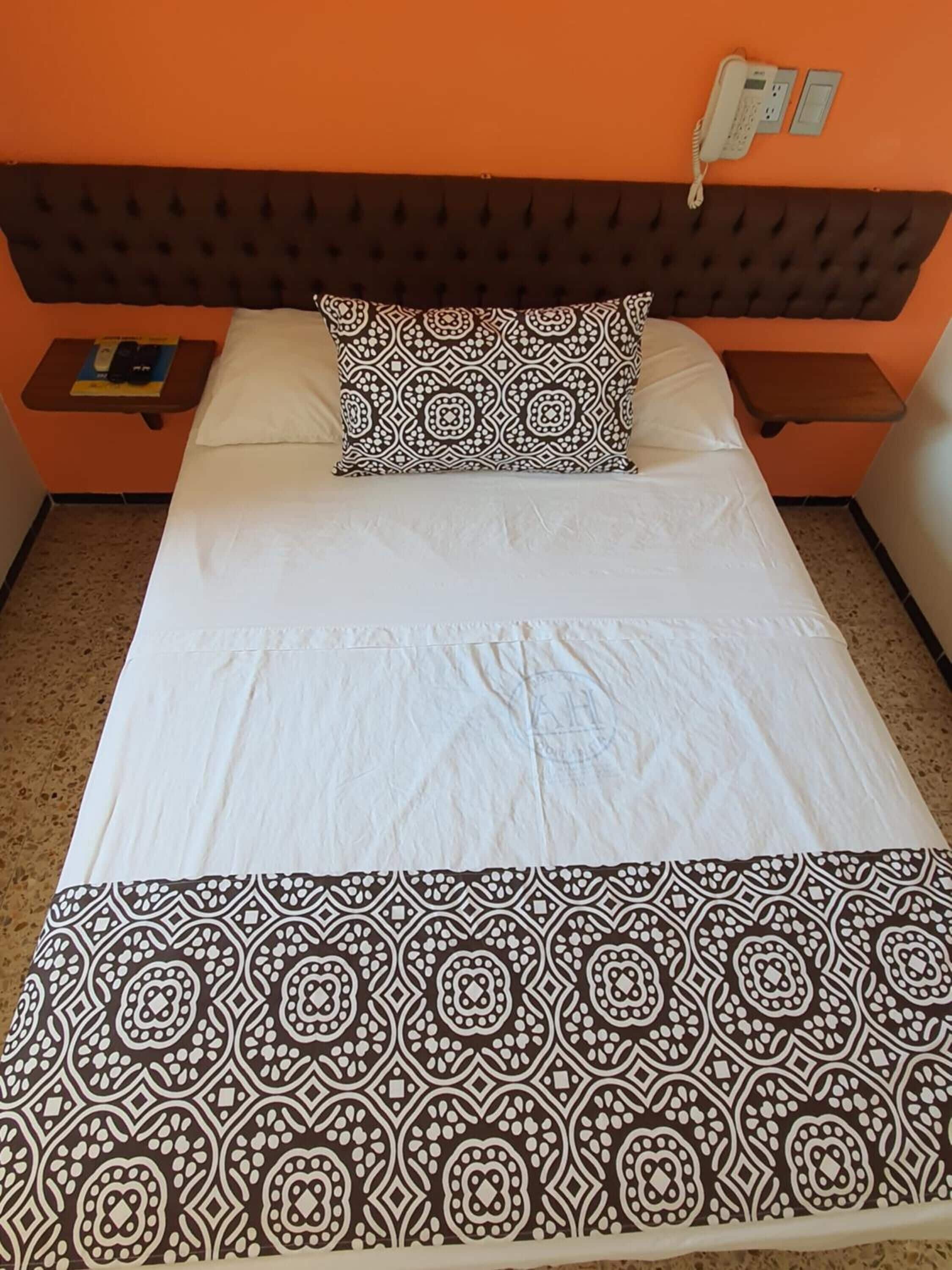 A bed with a patterned bedspread and pillow, two bedside tables, and a wall-mounted phone.