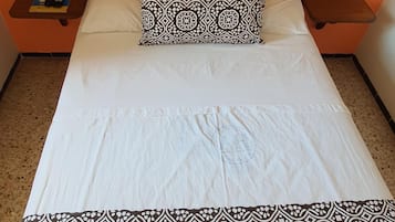 A bed with a patterned bedspread and pillow, two bedside tables, and a wall-mounted phone.