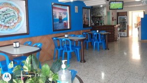 A restaurant interior with blue walls, multiple tables and chairs, a bar area, and a television screen displaying a sports game. - Hotel Atlantico (Veracruz)