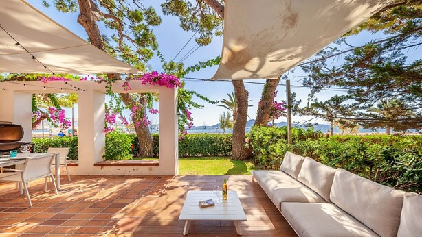 Eine Terrasse im Freien mit einem weißen Tisch, einer Couch und einem Grill.