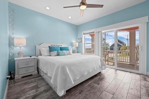 Relax in this serene bedroom with a large bed, ceiling fan, and balcony offering a view of the surrounding area.