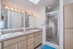 A modern bathroom with two sinks, a large mirror with lights, and a walk-in shower. - Salt Air (Depoe Bay)