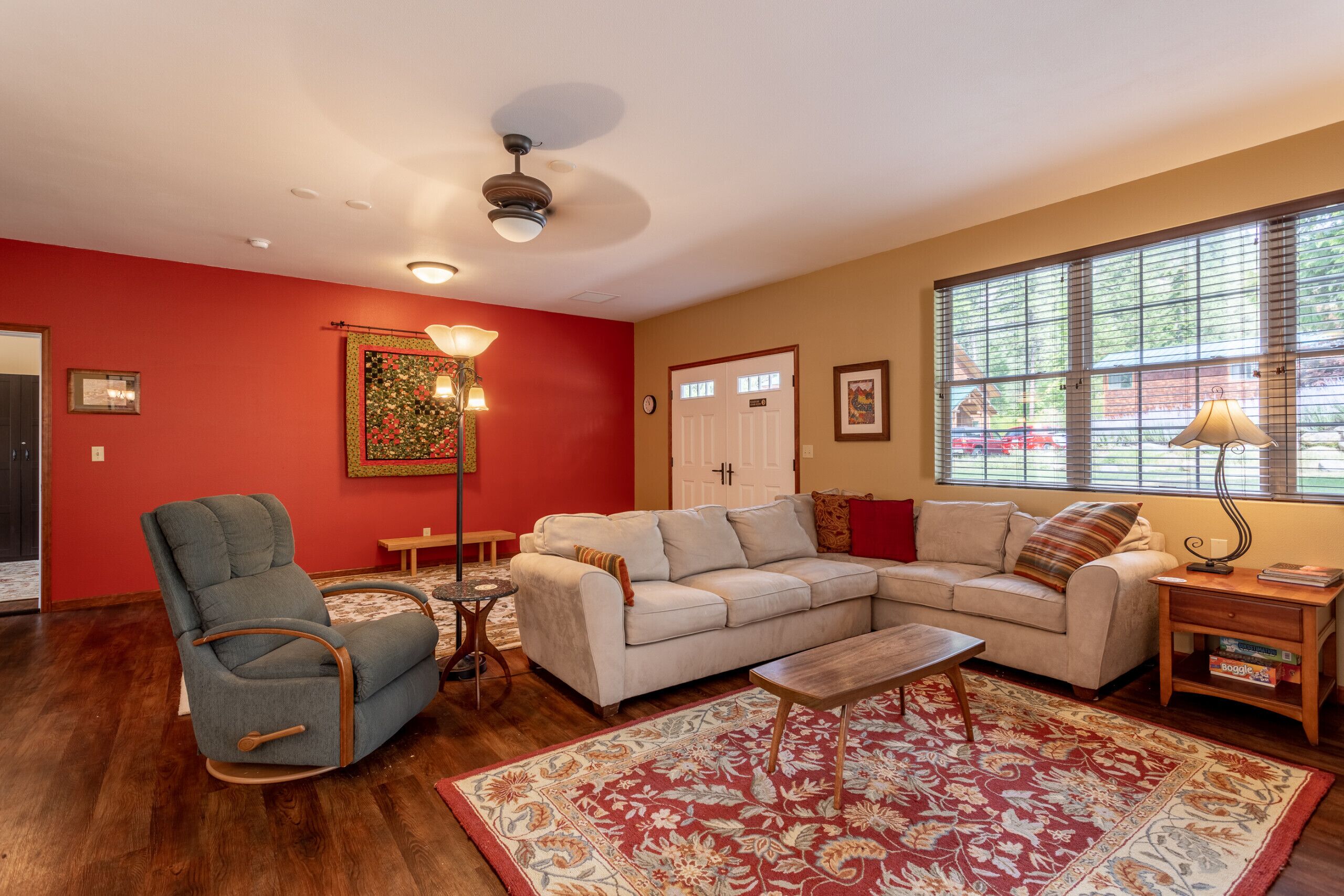A living room with a sectional sofa, a rocking chair, a coffee table, and a large window with blinds.
