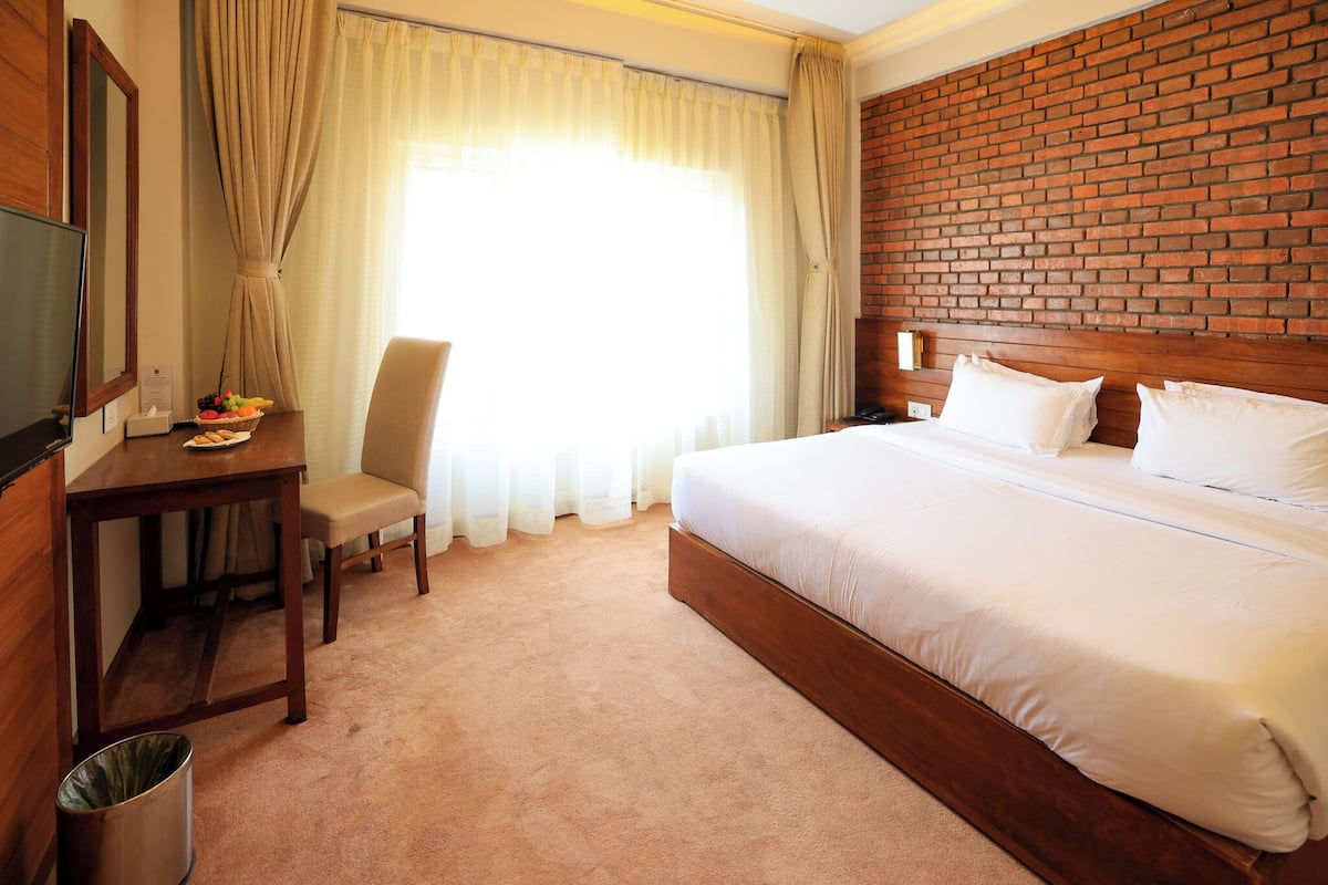 A hotel room with a large bed, a wooden desk with a chair, a TV, and a brick accent wall.