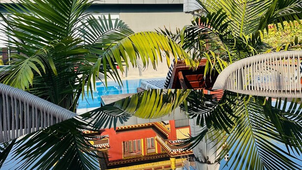 Un edificio tradicional con fachada roja y amarilla, una piscina reflectante y palmeras.