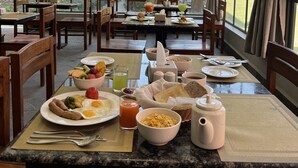 Comedor con mesas preparadas para el desayuno, con platos de huevos, tostadas y fruta.