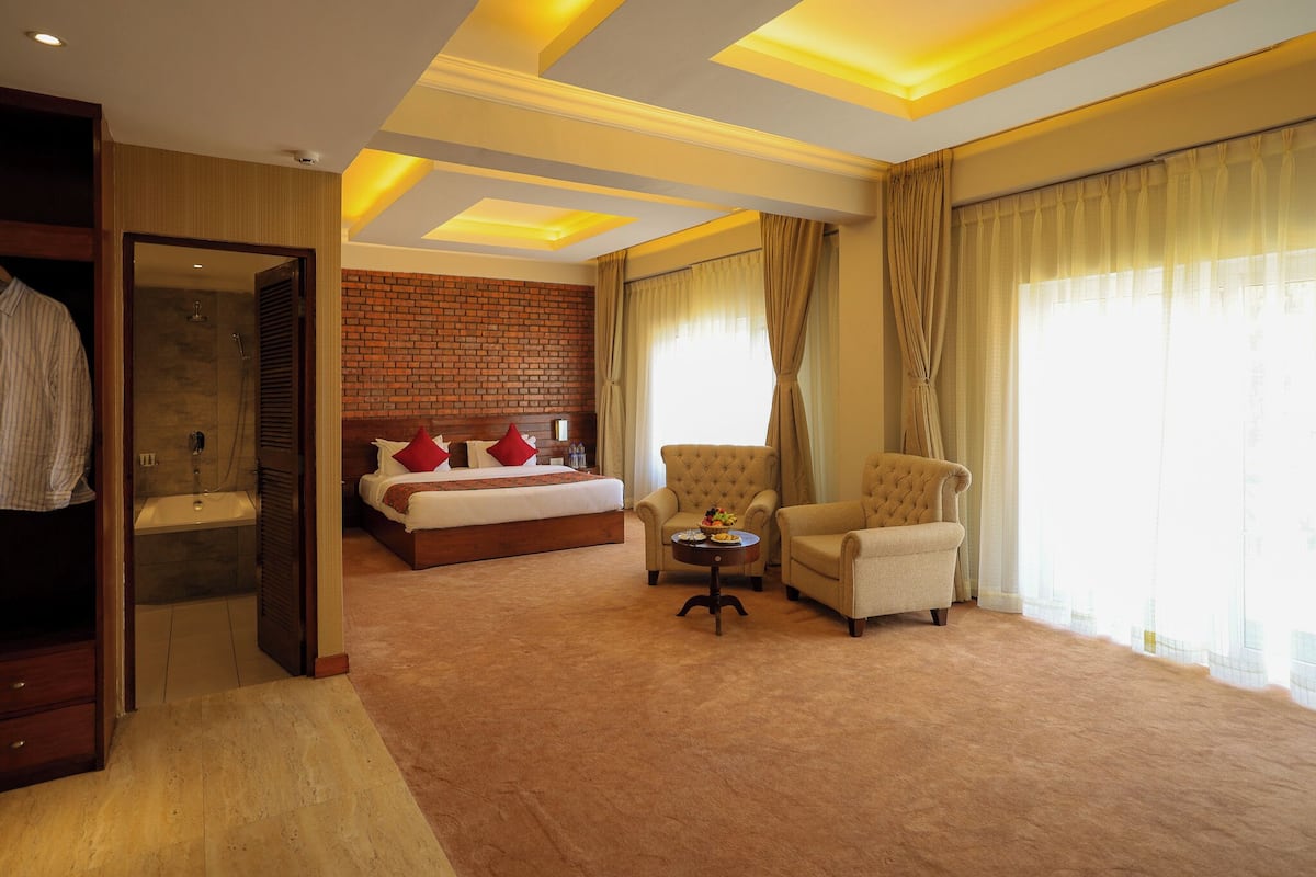 A hotel room with a large bed, two armchairs, a small table, and a bathroom with a sink and shower.