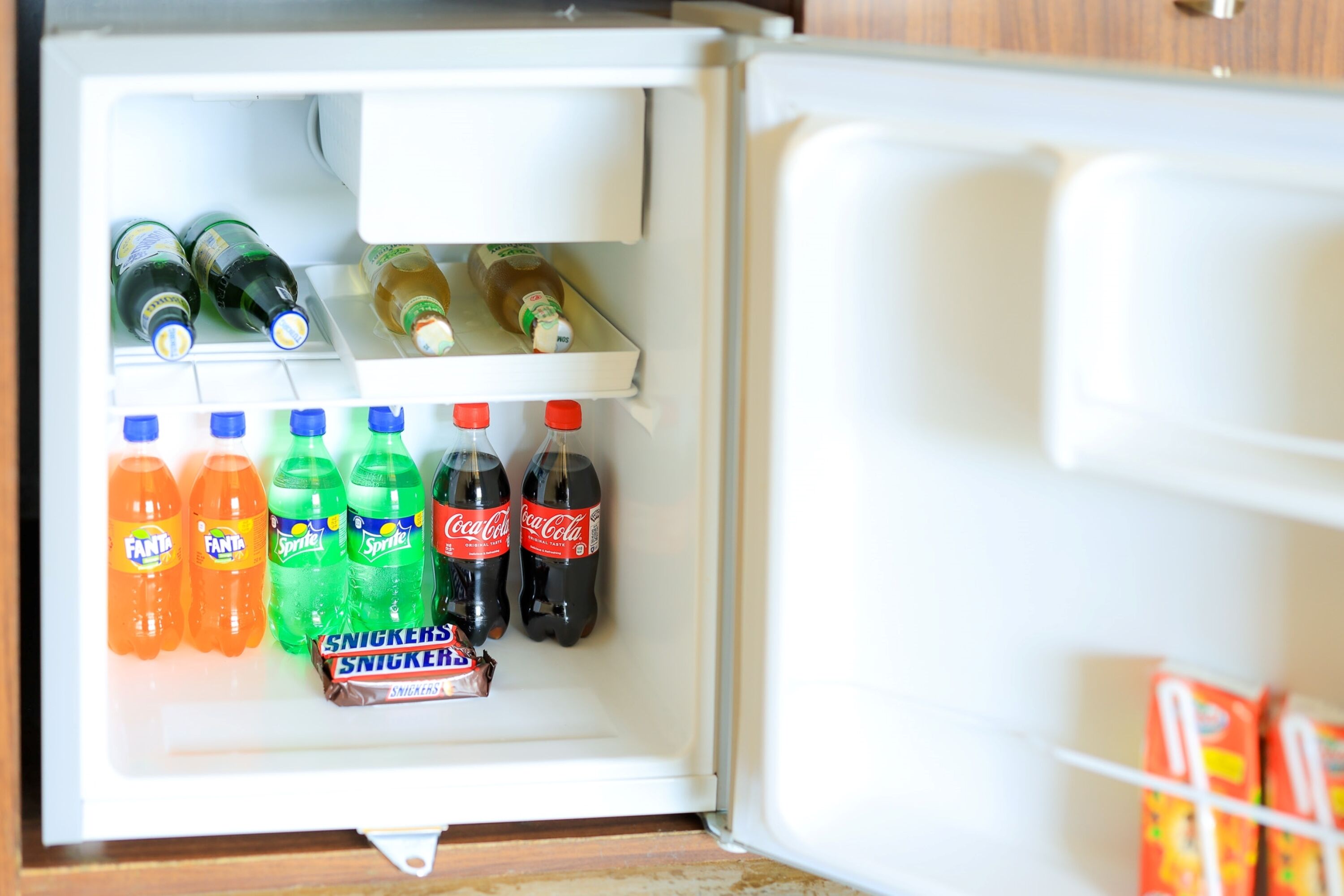 Un refrigerador lleno de diversas bebidas como Fanta, Sprite, Coca-Cola y Snickers.
